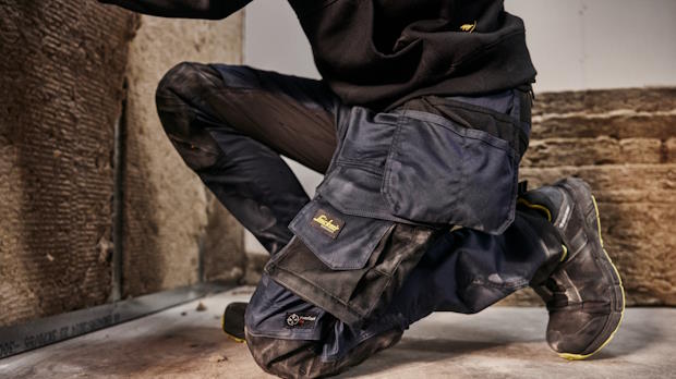 Bouwvakker in knielende houding in een werkbroek met ingebouwde kniebeschermers